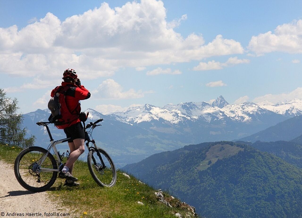 Mann mit Mountainbike steht auf einem Berg und guckt in die Ferne